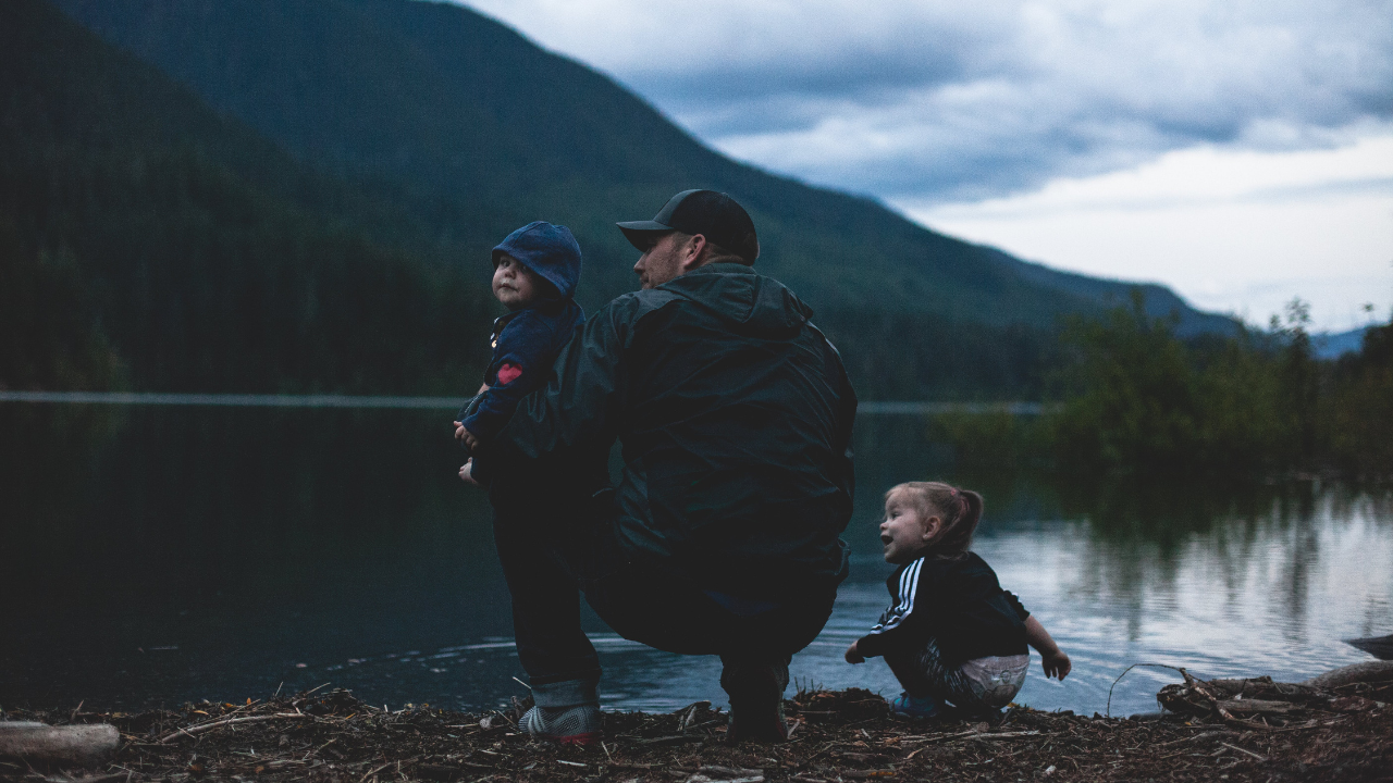 A father with two young children in front of a lake.